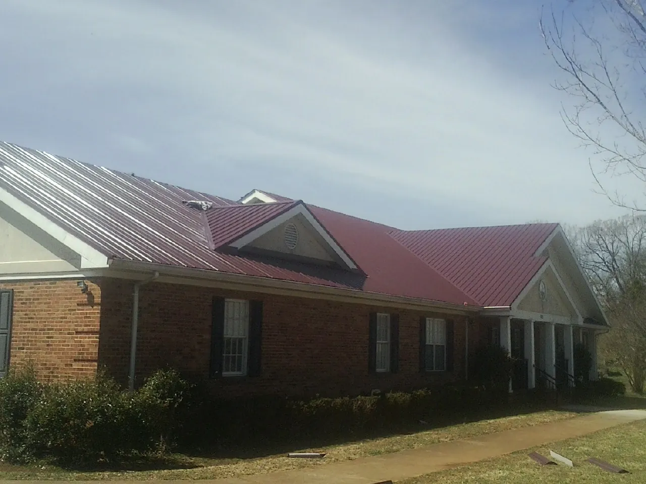 Red metal roof with gabled entries on a long brick building, from a Hail Damage Roof Repair job in Devine