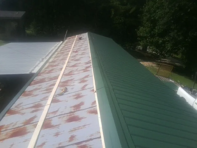 Old rusted panels beside newly installed green metal roofing — Wind Damage Roof Repair by Roofing Brothers in Devine