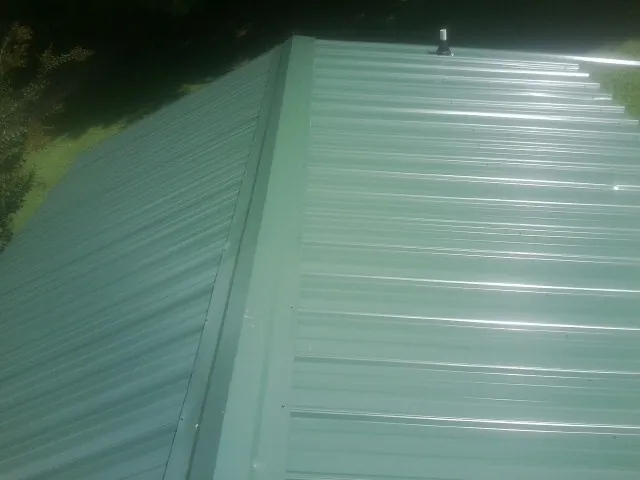 New green metal panels meeting at the ridge of a roof — Flat Roof Repair work by our crew in Devine