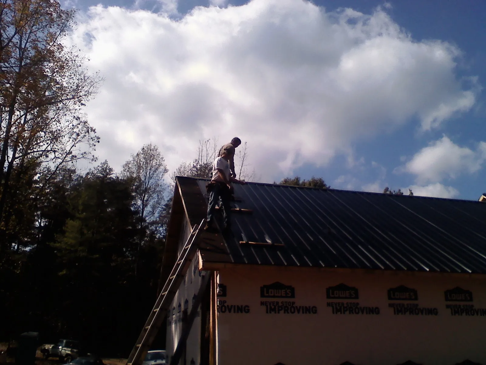 Roofer fastening dark metal panels high against a cloudy sky, from a Roof Inspection job in Devine